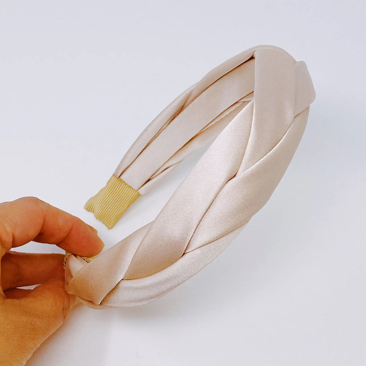 Beige headband with gold clip held by a hand on a light background